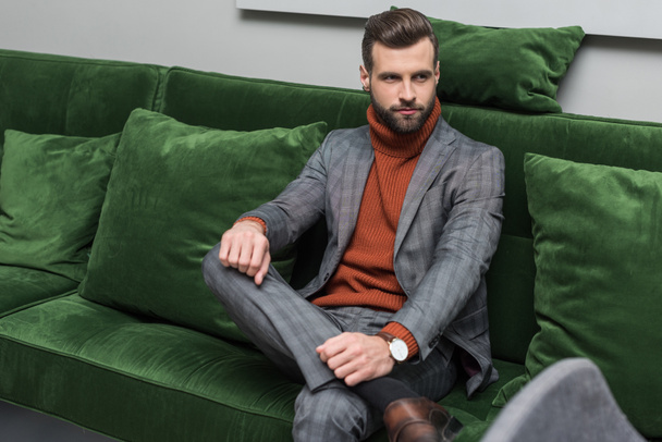 man in formal wear with legs crossed sitting on green sofa - Fotoğraf, Görsel