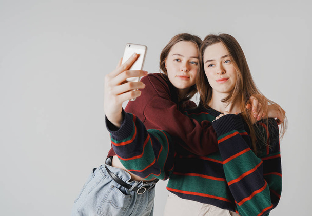 Twee zussen twins mooie meisjes in casual doen selfie op smartphone op grijze achtergrond geïsoleerd - Foto, afbeelding