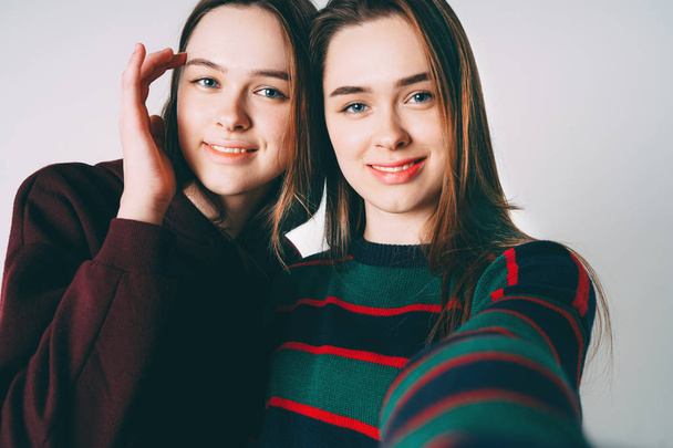Two sisters twins beautiful girls in casual clothes taking selfie on frontal camera of smartphone on grey background isolated - Foto, afbeelding