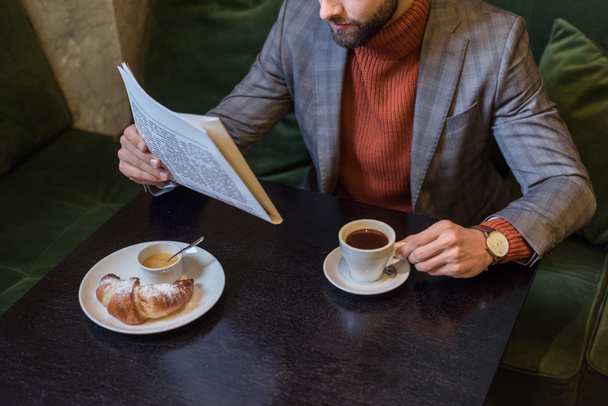 vista recortada de un hombre elegante en ropa formal sentado en la mesa y leyendo el periódico en el restaurante
 - Foto, imagen