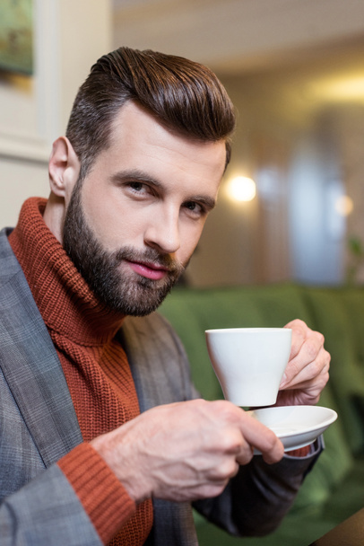 handsome man in formal wear looking at camera and drinking coffee in restaurant - Φωτογραφία, εικόνα