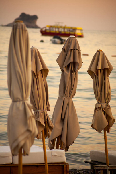 Закриті парасольки сонця, подорожі на човні на горизонті, захід сонця на тлі спокійного моря
 - Фото, зображення