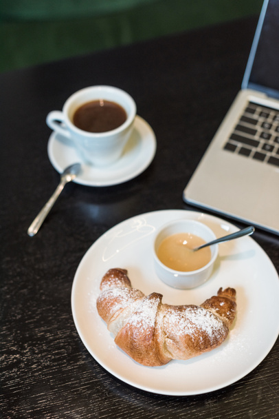 piatto con croissant e salsa, caffè e laptop sul tavolo nel caffè
 - Foto, immagini