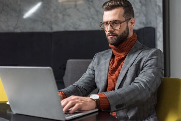 красивый бизнесмен в формальной одежде и очках сидит за столом и печатает на ноутбуке в ресторане
 - Фото, изображение