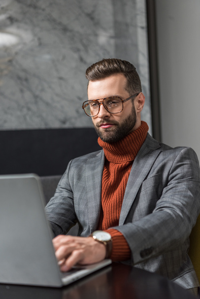 целенаправленный красивый бизнесмен в формальной одежде и очках сидит за столом и печатает на ноутбуке в ресторане
 - Фото, изображение