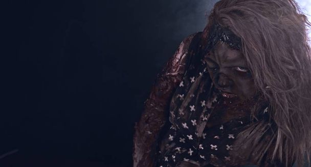 Creepy zombie woman posing against dark misty background - Foto, Imagen