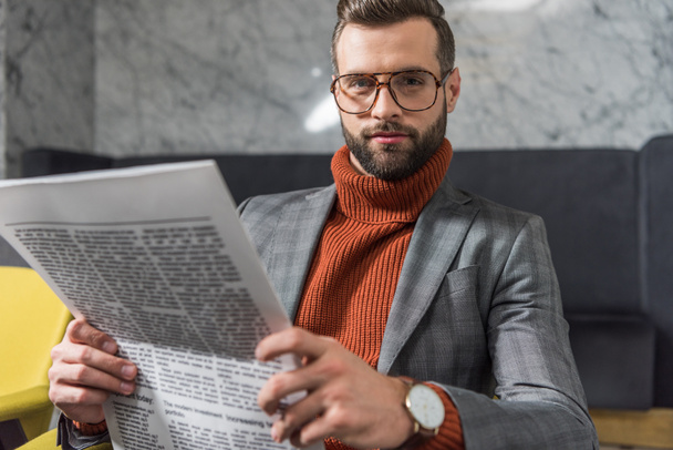 stylish man in formal wear looking at camera and holding newspaper in restaurant - Φωτογραφία, εικόνα