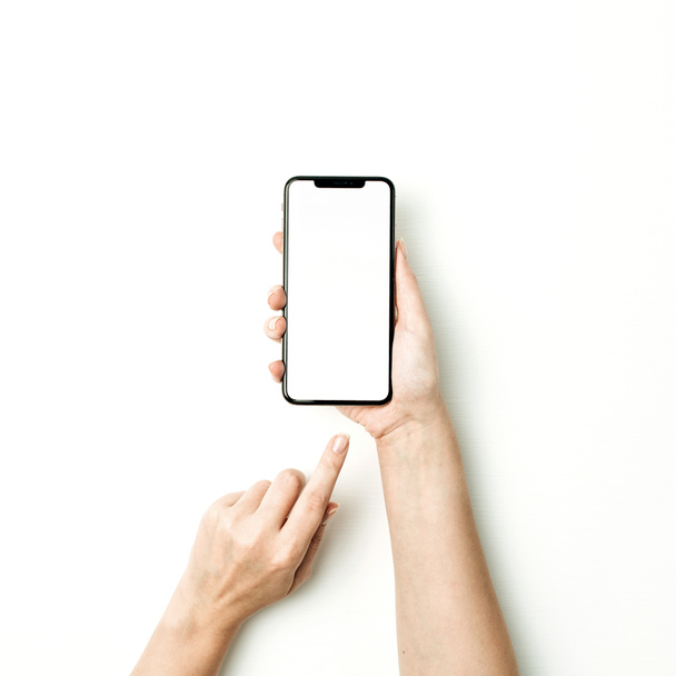 Donna che tocca lo schermo bianco del nuovo modello di smartphone su sfondo bianco. Piatto lay, vista dall'alto mockup
. - Foto, immagini