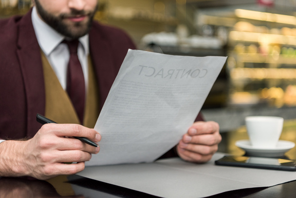 cropped view of businessman in formal wear sitting at table and looking at contract - Фото, зображення