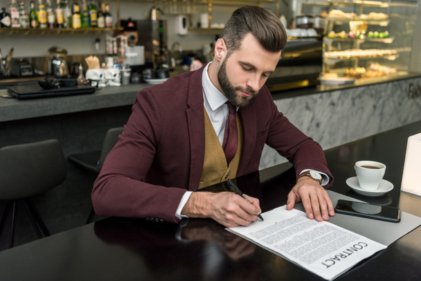 guapo hombre de negocios en ropa formal sentado en la mesa y la firma de contrato
  - Foto, Imagen