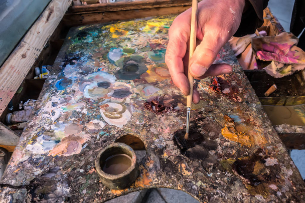 Primer plano de la mano del artista con un pincel mezcla pintura en la paleta
. - Foto, Imagen