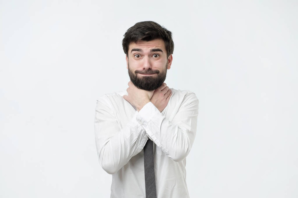 spanischer Mann mit Bart und weißem Hemd, der vor grauem Hintergrund die Hände am Hals hält - Foto, Bild