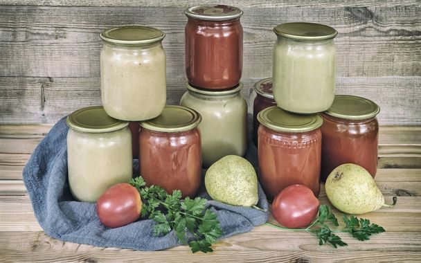 Pyré a rajčatové šťávy z hrušek jsou zachovány ve sklenicích s uzavřených kovových víček. Poblíž lež hrušky a rajčata. - Fotografie, Obrázek