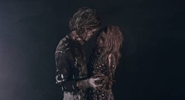 portrait of tender zombie couple hugging together against dark background - Photo, image
