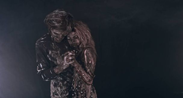 portrait of tender zombie couple hugging together against dark background - Photo, image