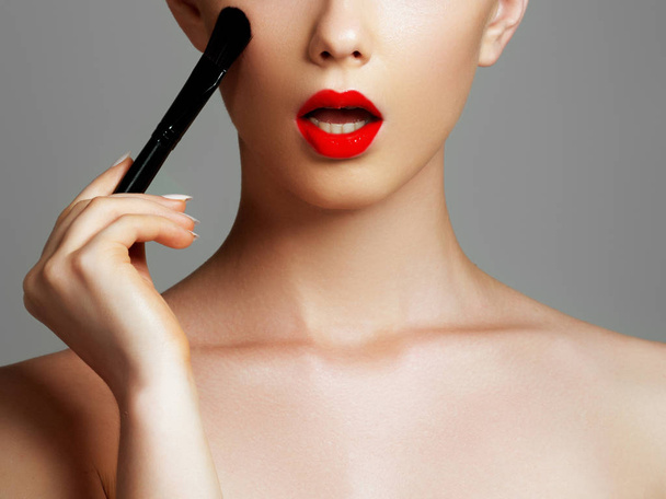Beauty face. Makeup artist concept. Cute girl applies red lipstick . Beautiful woman face. Make-up master, painting lips of young beauty model girl. Make up in process - Photo, Image