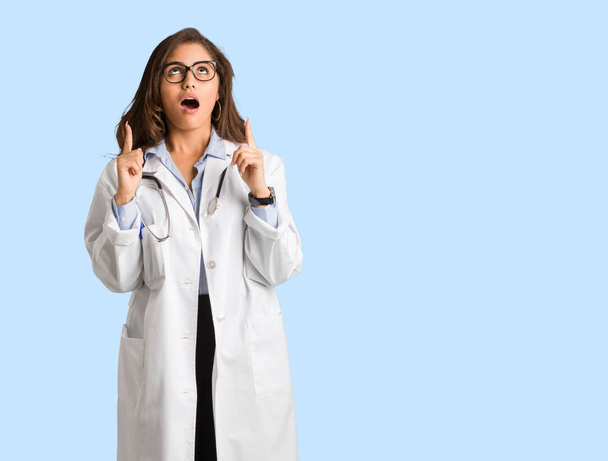 Full body young doctor woman surprised pointing up to show something - Photo, Image