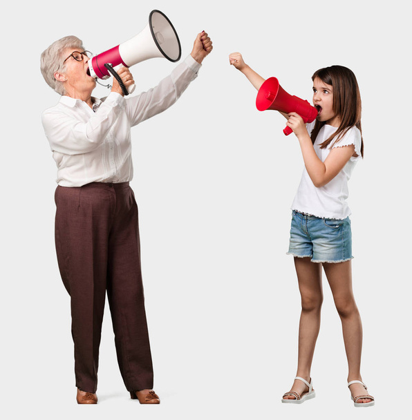 Corpo inteiro de uma senhora idosa e sua neta animado e eufórico, gritando com um megafone, sinal de revolução e mudança, incentivando outras pessoas a se mover, personalidade líder
 - Foto, Imagem