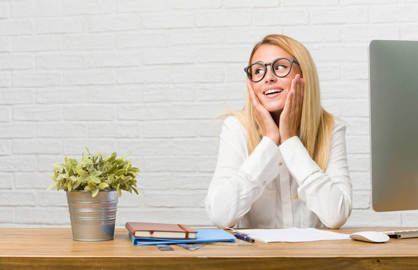 Portrait of young student sitting on her desk doing tasks surprised and shocked, looking with wide eyes, excited by an offer or by a new job, win concept - Photo, Image