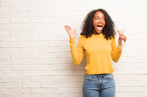 Jonge zwarte vrouw schreeuwen blij verrast door een aanbieding of promotie, gapende, springen en trots - Foto, afbeelding
