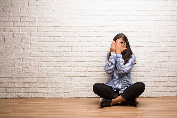 Jeune femme indienne assise contre un mur de briques se sent inquiète et effrayée, regardant et couvrant le visage, concept de peur et d'anxiété
 - Photo, image