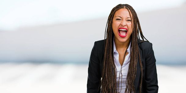 Retrato de una joven mujer de negocios negra gritando enojada, expresión de locura e inestabilidad mental, boca abierta y ojos medio abiertos, concepto de locura
 - Foto, Imagen