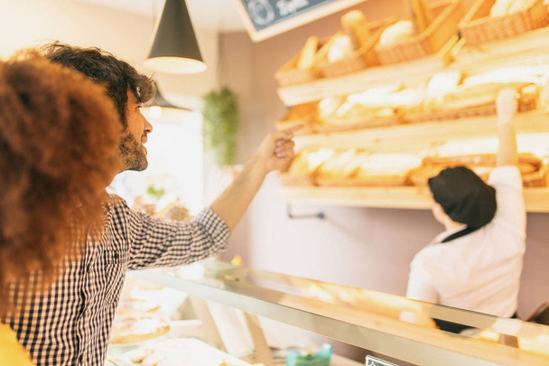 Young modern couple at bakery, choosing a loaf of bread. - 写真・画像
