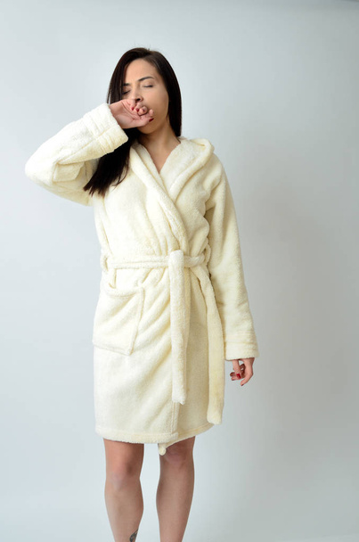 Young female wearing dressing-gown with white background. Awaking in the morning, stretching and yawning.  - Фото, изображение