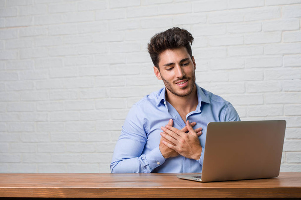 Молодой бизнесмен сидит и работает на ноутбуке, делая романтический жест, влюбляясь в кого-то или проявляя привязанность к какому-то другу
 - Фото, изображение