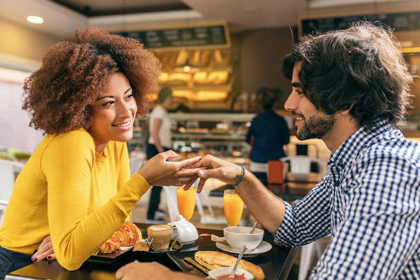 Mladý pár má na snídani v kavárně, sebe, hladí jejich rukou jsou v lásce, usmívající se a šťastné, těší ráno. - Fotografie, Obrázek