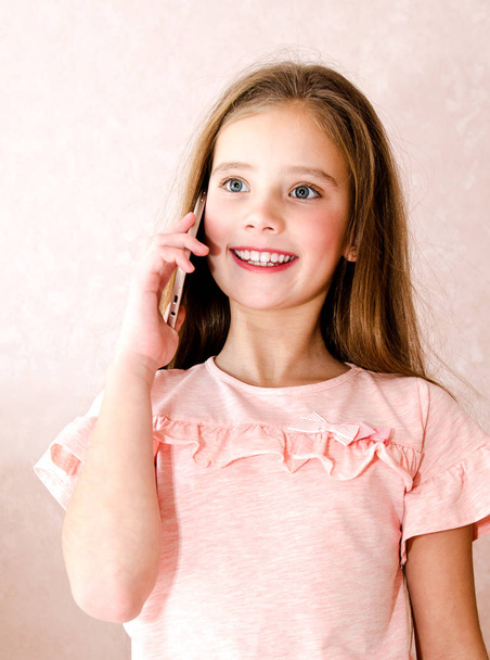 Портрет милой улыбающейся маленькой девочки, звонящей на мобильный телефон смартфон изолирован на розовом фоне
 - Фото, изображение