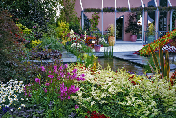 Modern ontworpen patio uitbreiding aan dek gebied en kleurrijke en goed geplant bloem randen rond een water-functie - Foto, afbeelding