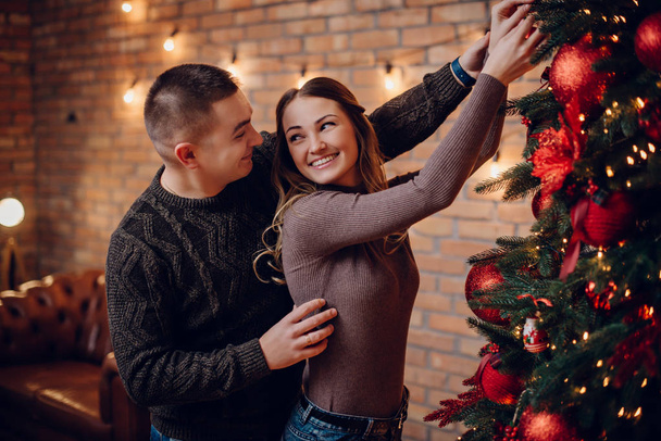 young couple decorating christmas tree together at home - Фото, изображение