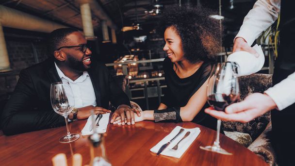 Waiter Pouring Wine to Glass Couple in Restaurant. Romantic African American Couple in Love Dating. Cheerful Man and Woman Drinking Red Wine. Romantic Concept. Anniversary. Bottle of Red Wine. - Zdjęcie, obraz