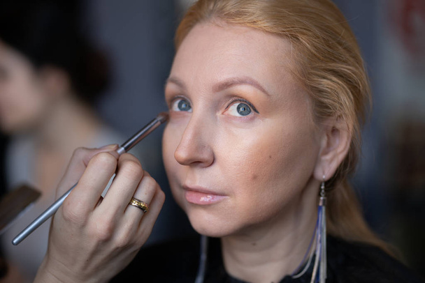 artista de maquillaje profesional aplica maquillaje paso a paso en la cara de una mujer rubia
 - Foto, Imagen