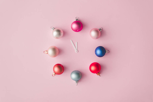 Clock hands with colorful pastel decoration balls on pink painted wall. Chrismas eve concept  - Photo, Image
