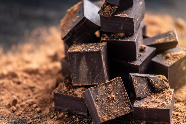 Trozos de chocolate amargo oscuro con cacao en polvo sobre fondo de madera oscura. El concepto de ingredientes de confitería
 - Foto, imagen