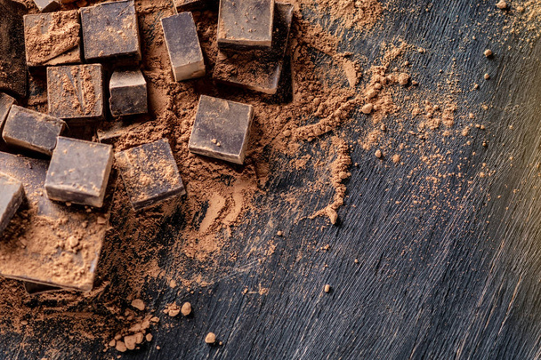Stücke dunkler Bitterschokolade mit Kakaopulver auf dunklem Holzgrund. Karte mit Platz für Text - Foto, Bild