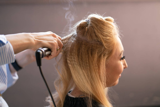 beautiful adult blonde client sits in a chair while a hairdresser master in the salon does her hair with a corrugation and a Perm - Photo, Image