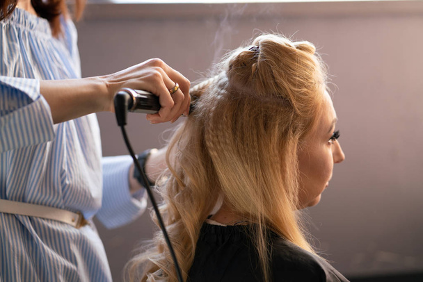 krásné dospělé blondýna klient sedí v křesle, zatímco mistr kadeřník v salonu dělá vlasy zvlnění a Perm - Fotografie, Obrázek