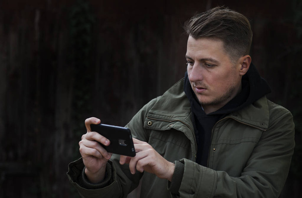 Portrait of young man isolated on gray background, looking agitated at display of her smartphone, impressed by media content from web - Zdjęcie, obraz