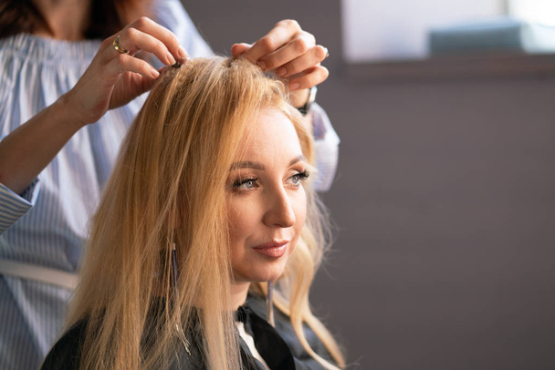 beautiful adult blonde client sits in a chair while a hairdresser master in the salon does her hair with a corrugation and a Perm - Fotografie, Obrázek