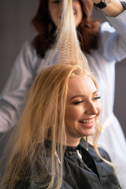 belle cliente blonde adulte s'assoit sur une chaise tandis qu'un coiffeur maître dans le salon fait ses cheveux avec une ondulation et un Perm
 - Photo, image