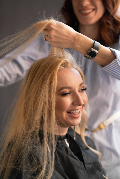 krásné dospělé blondýna klient sedí v křesle, zatímco mistr kadeřník v salonu dělá vlasy zvlnění a Perm - Fotografie, Obrázek
