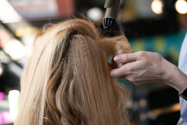 美しいアダルト金髪クライアント サロンで美容師のマスターは、段ボールとパーマ髪の椅子に座っています。 - 写真・画像