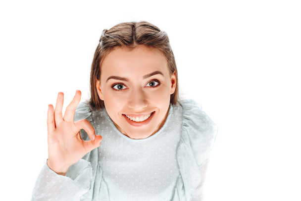 Hochwinkel-Ansicht der attraktiven lächelnden Frau zeigt ok Zeichen isoliert auf weiß - Foto, Bild