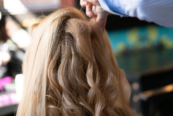 hermosa cliente rubia adulta se sienta en una silla, mientras que un maestro de peluquería en el salón hace su cabello con una ondulación y una permanente
 - Foto, imagen