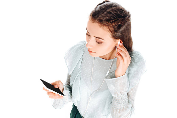 vista ad alto angolo di donna utilizzando smartphone durante l'ascolto di musica in auricolari isolati su bianco
 - Foto, immagini