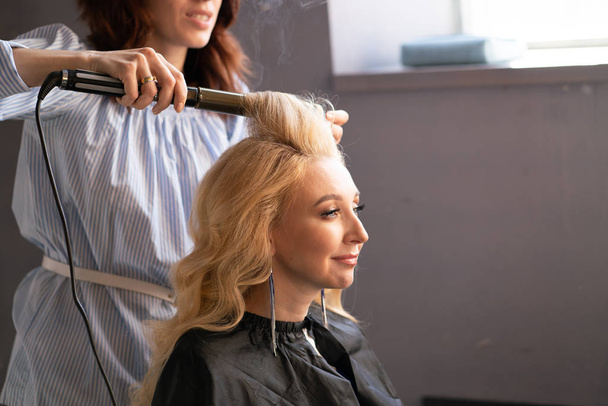 piękna dla dorosłych Blondynka klient siedzi na krześle, a mistrzem fryzjera w salonie czy jej włosy z falistego i Perm - Zdjęcie, obraz