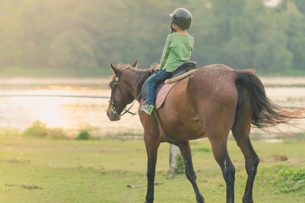 Діти вчаться кататися на коні біля річки перед заходом сонця
. - Фото, зображення